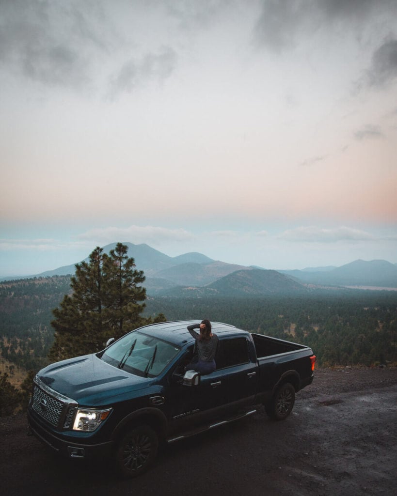 female sitting in a blue truck watching sunset over San francisco peaks flagstaff az