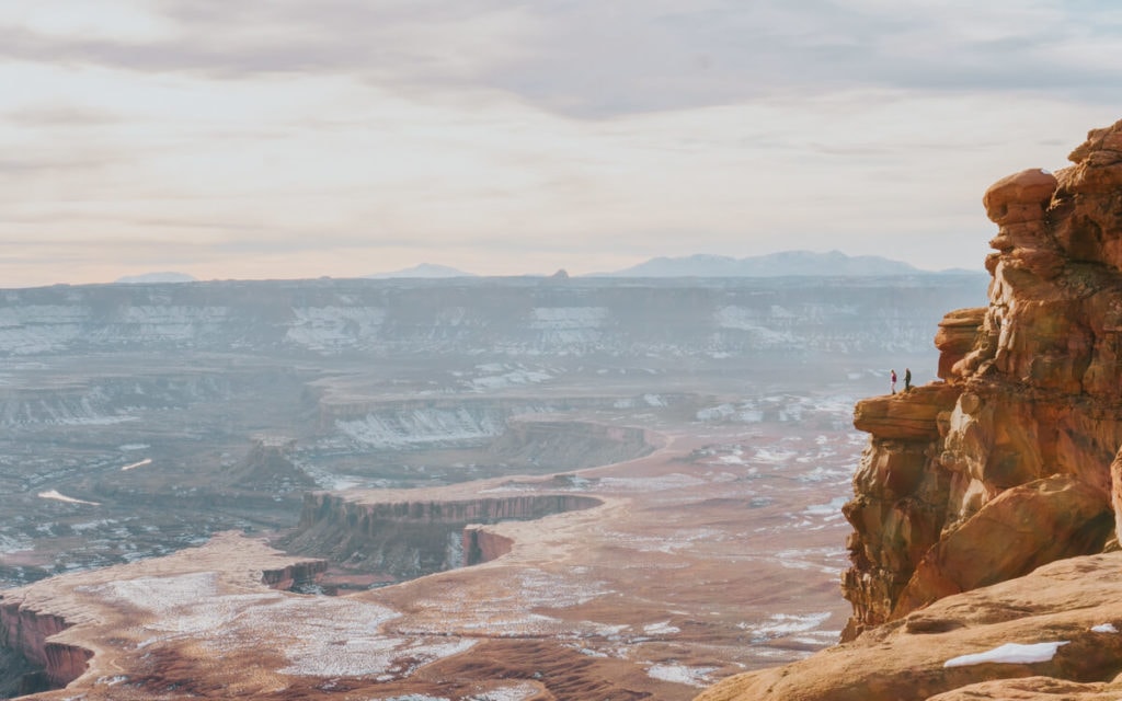 two female hikers watching a pink sunset from green river overlook in canyonlands national park utah