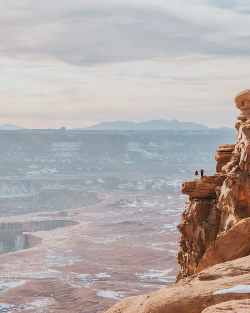 two female hikers watching a pink sunset from green river overlook in canyonlands national park utah
