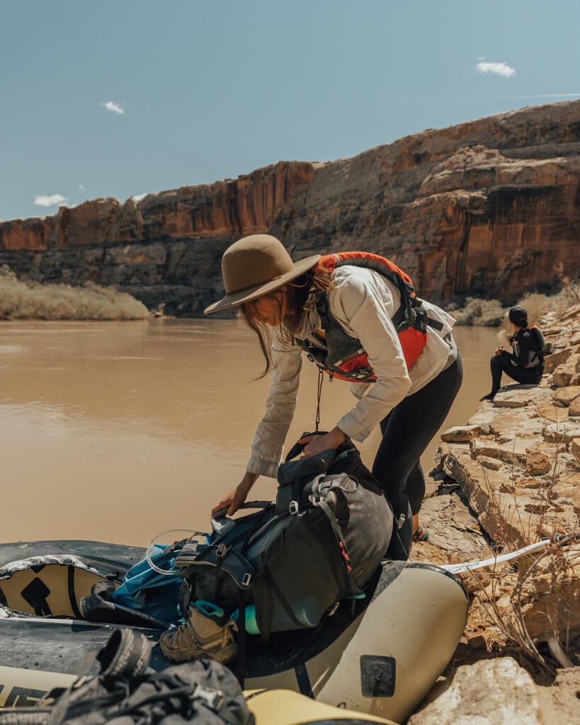 female loading a backpack onto a packraft on canyonland's green river