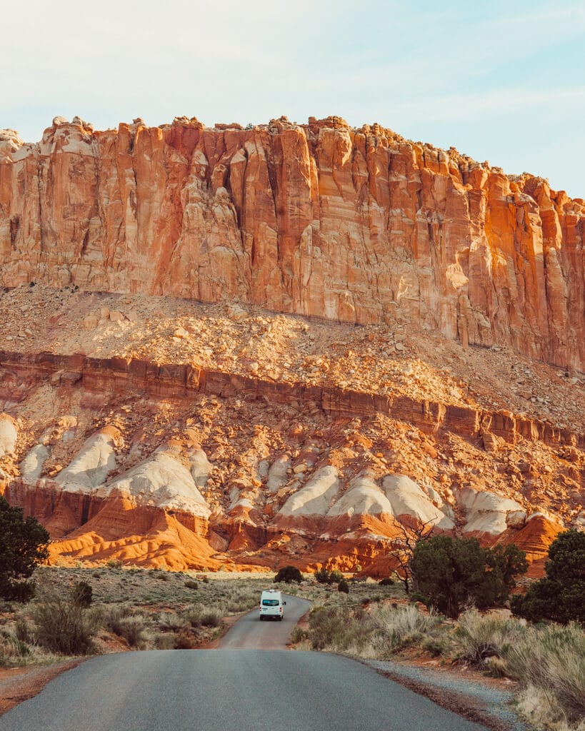 white campervan driving down the scenic drive towards an orange canyon in capitol reef national park utah