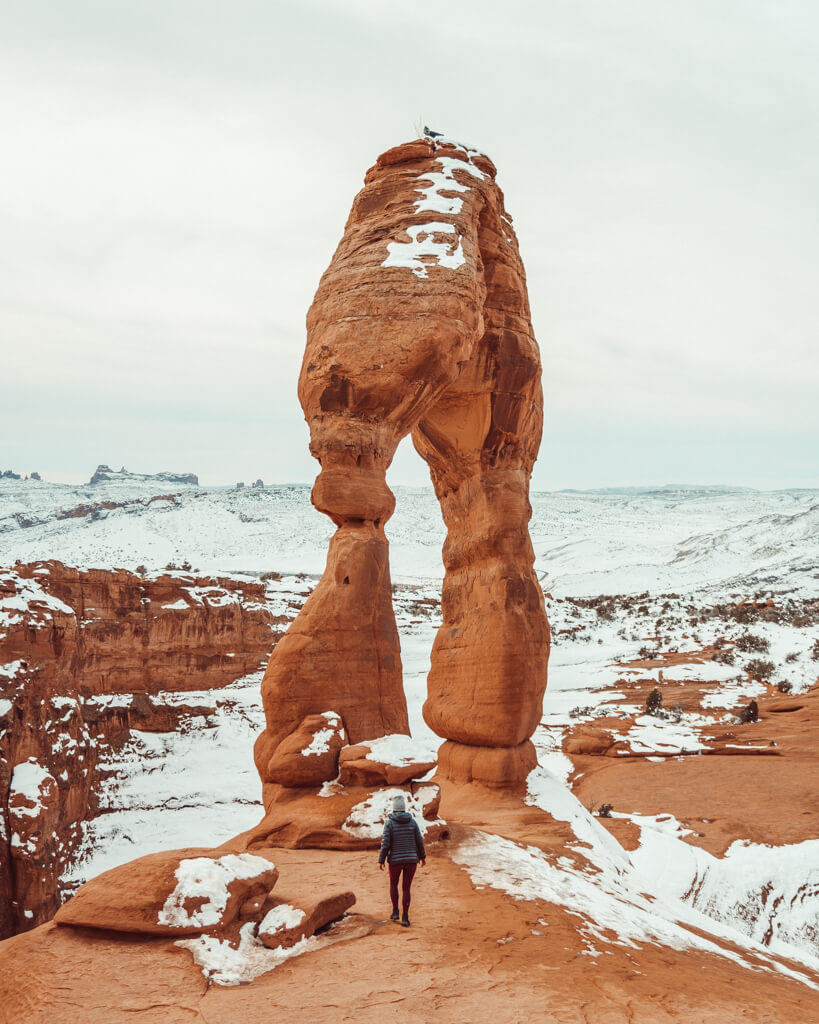 female hiker watching sunrise over delicate arch in arches national park utah on a winter morining