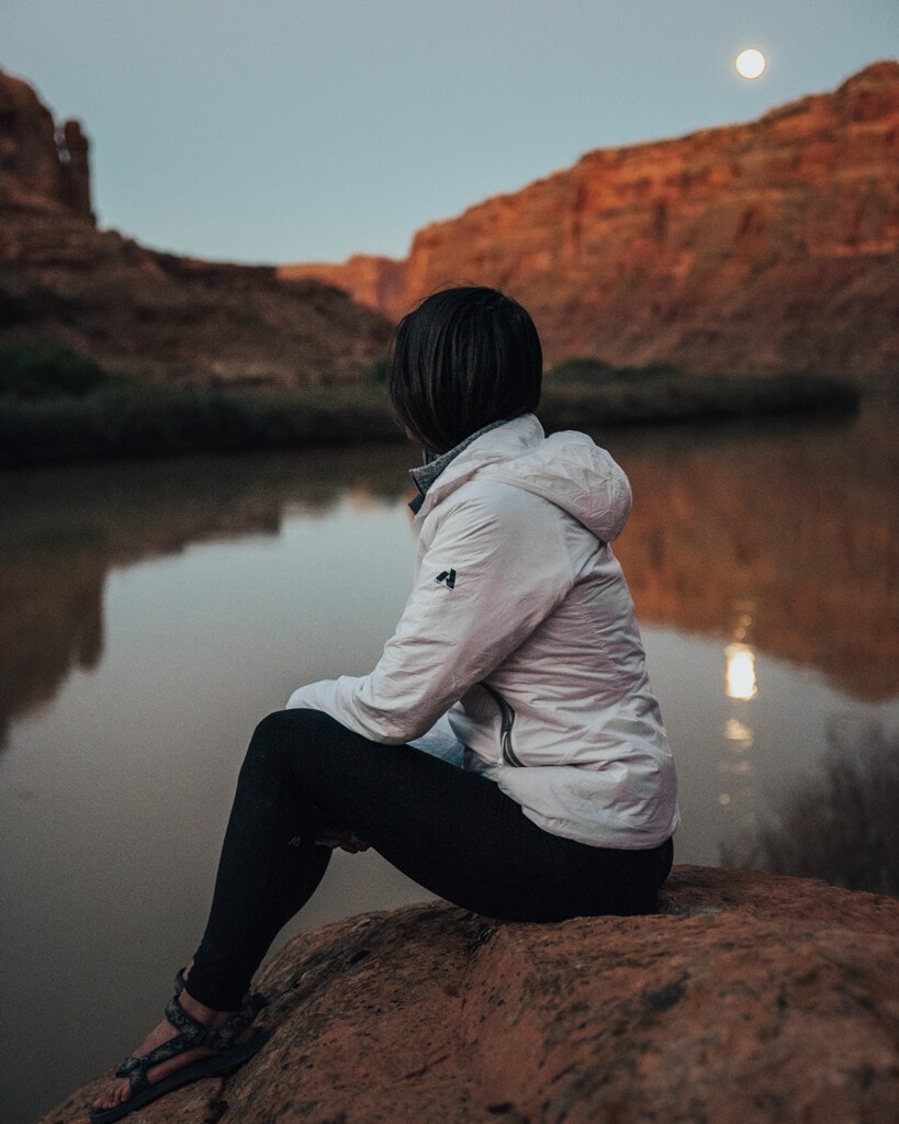 female in a white jacket looking at the moon in canyonlands national park