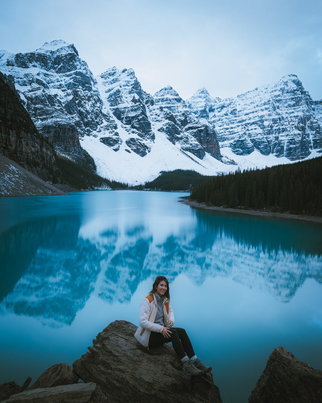 female hiker sitting in front of lake moraine in banff in winter