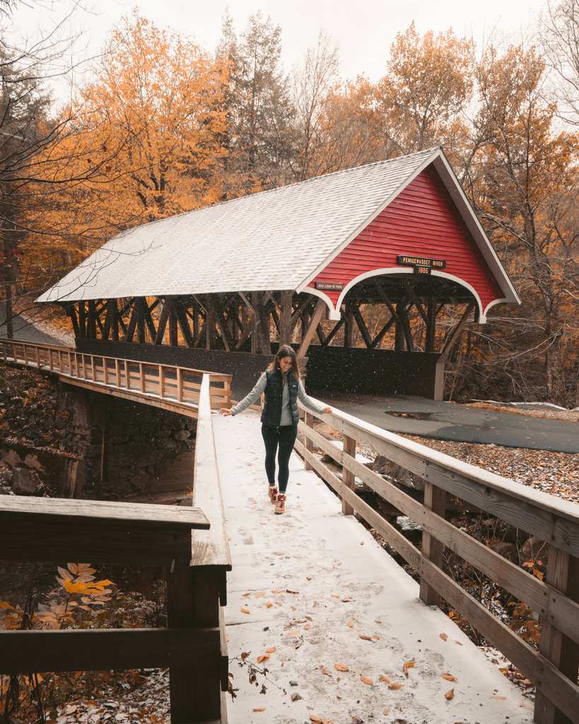 female hiker walking under red Flume Gorge covered bridge in the fall