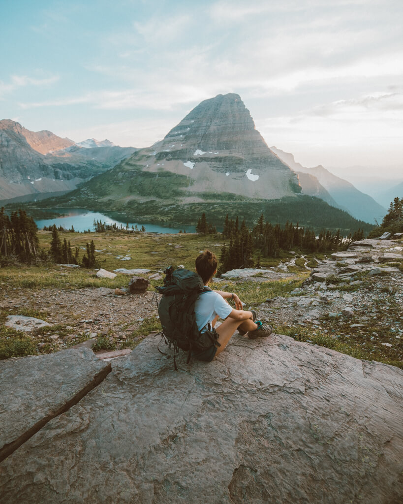 female hiker watching sunset over Hidden Lake Overlook in Glacier National Park on a sunny day