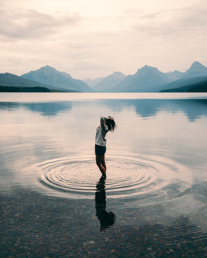 female standing in the crystal clear waters of lake mcdonald in glacier national park during sunrise
