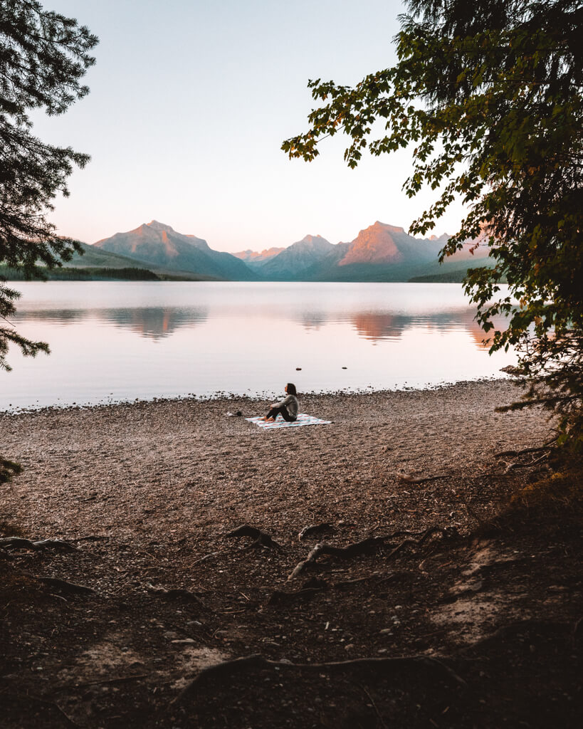female sitting on a blanket watching a pink sunset over lake mcdonald during a glacier national park itinerary
