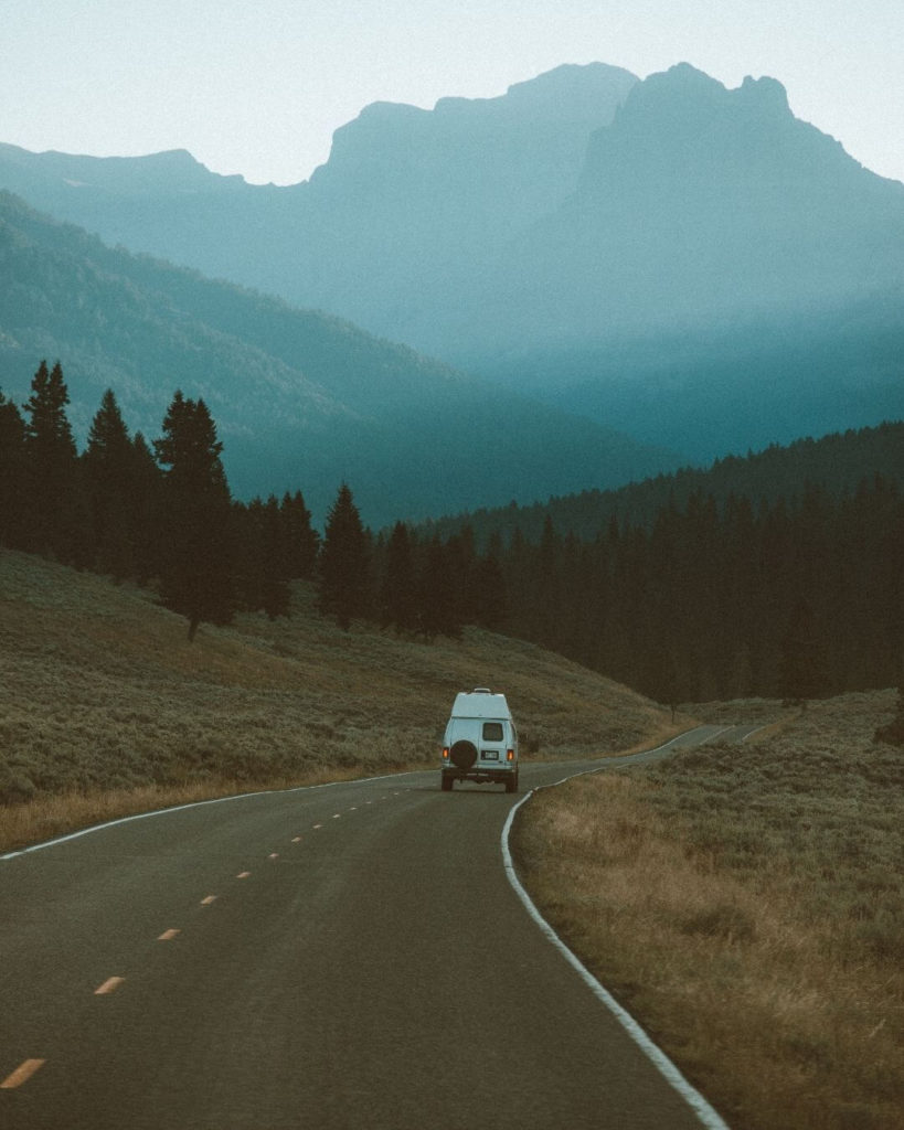 view of a campervan driving down a road with a mountain view in yellowstone national park