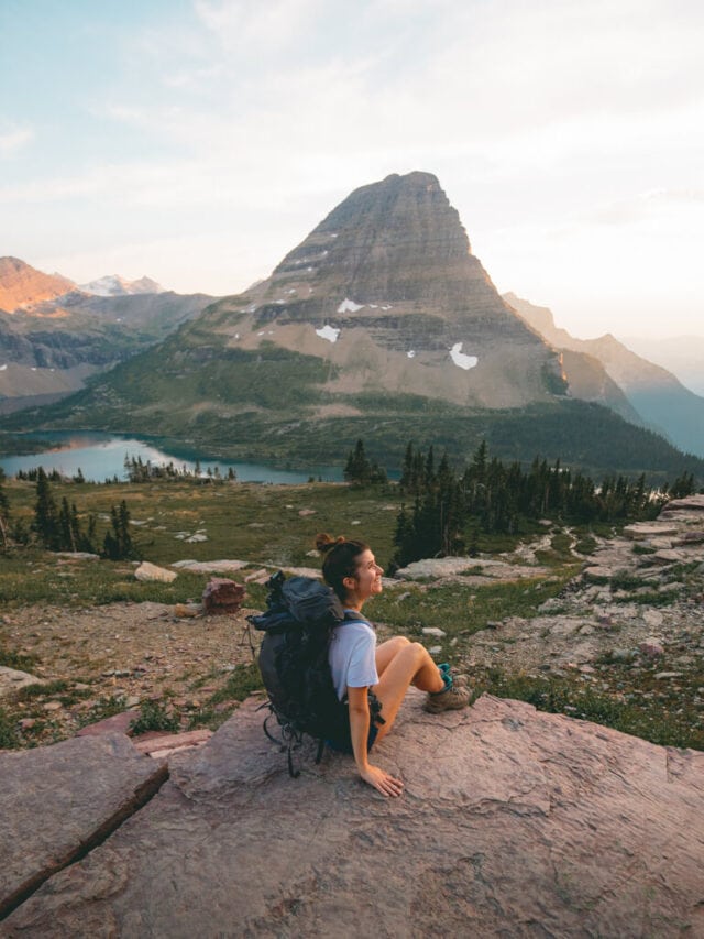 female hiker watching a pink sunset over Hidden Lake Overlook Trail in glacier national park montana
