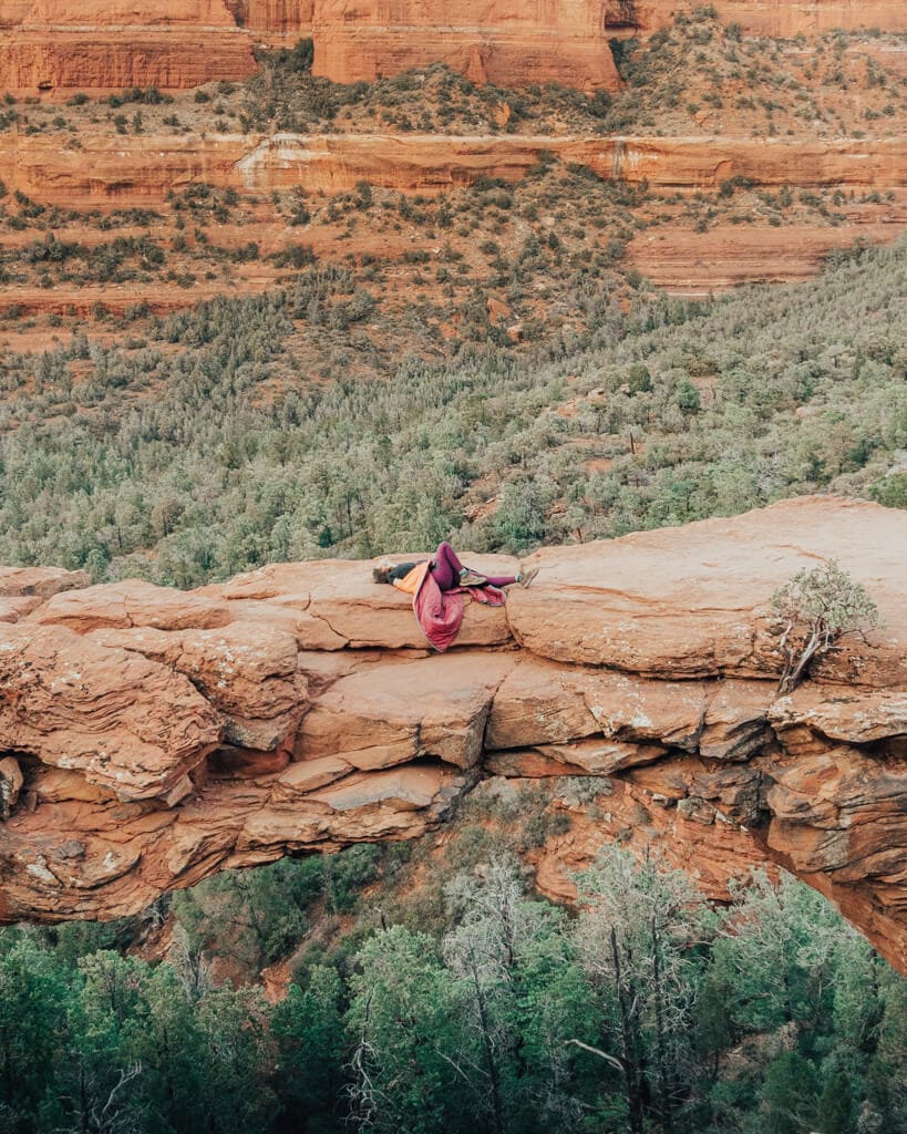 female hiker laying down on devil's bridge sedona az looking at red rocks