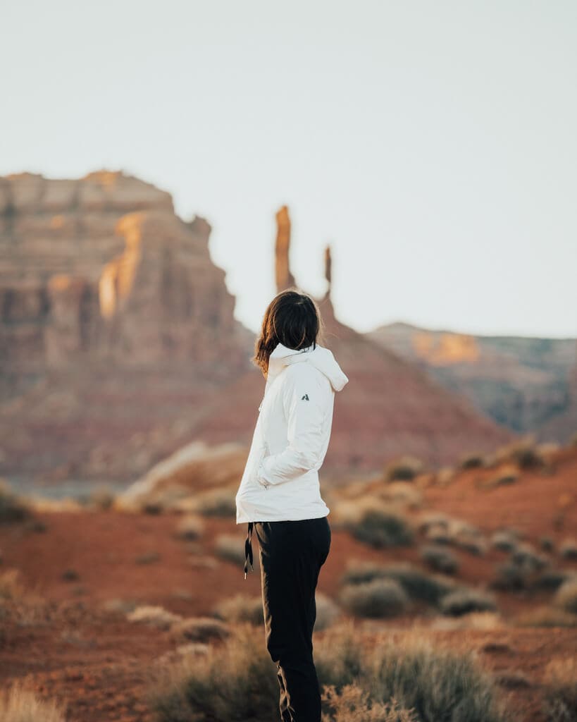 female in a white jacket looking at the sunset over valley of the gods utah