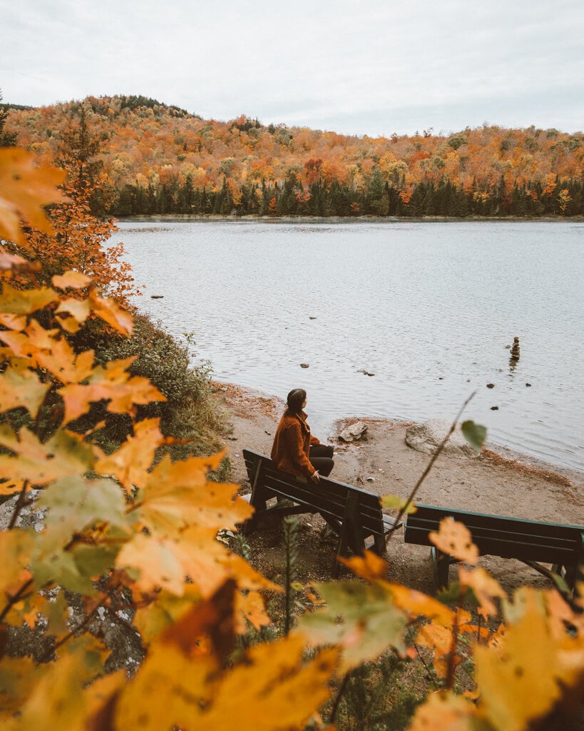 girl sitting on a bench surrounded by orange fall foliage in lake placid ny
