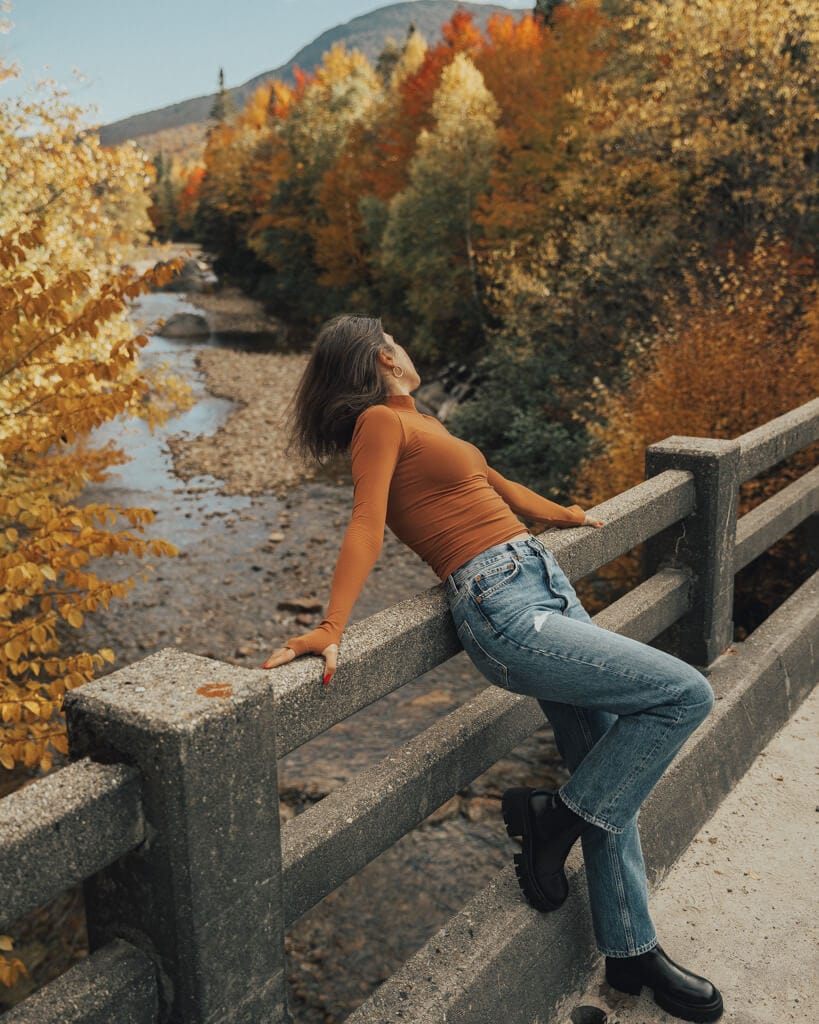 female wearing an orange turtle neck looking at the gold fall foliage along the saco river nh
