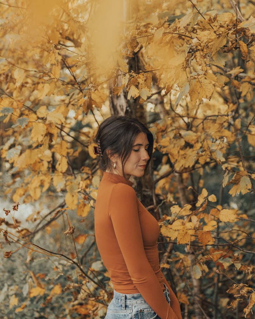 female wearing an orange turtle neck standing near orange fall foliage in echo lake new hampshire