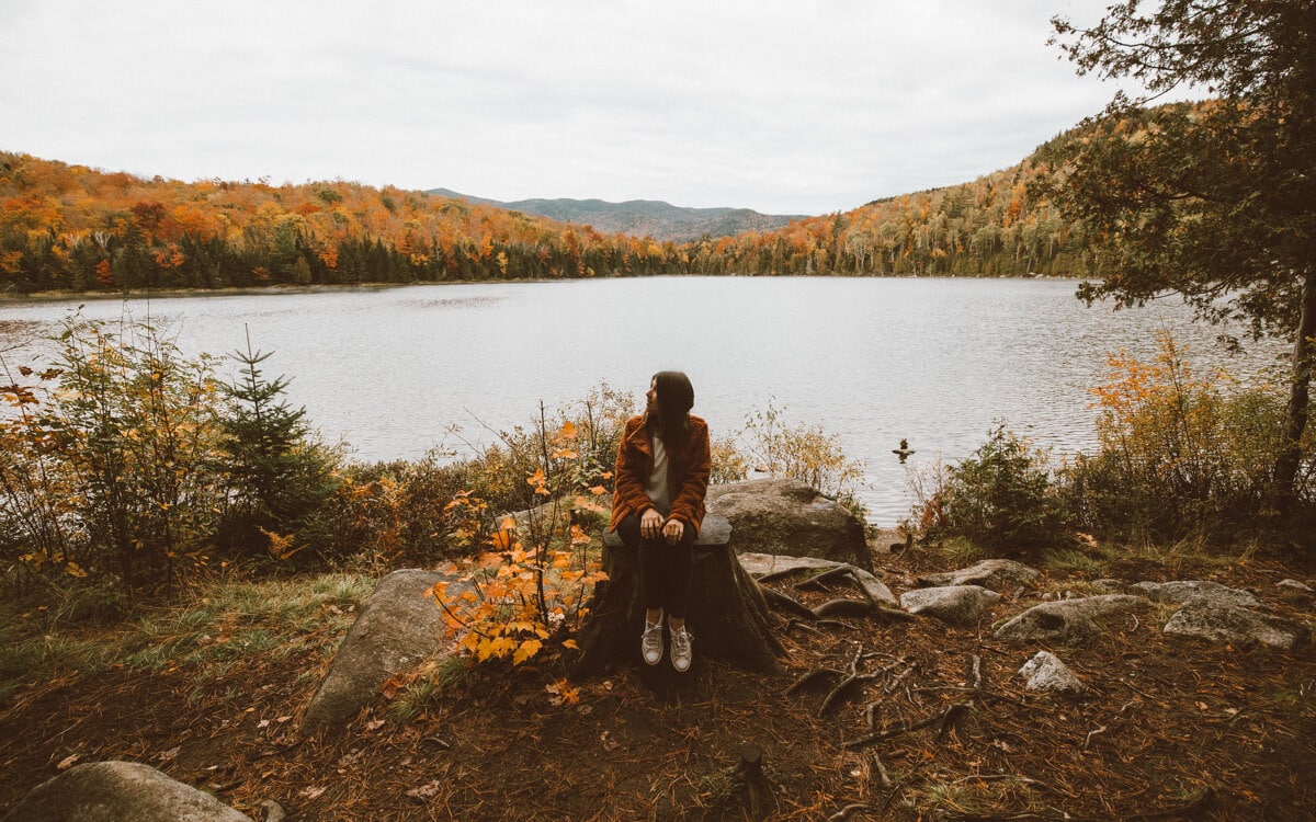 girl sitting on a log on the beach at the adirondack mountains heart lake in the fall