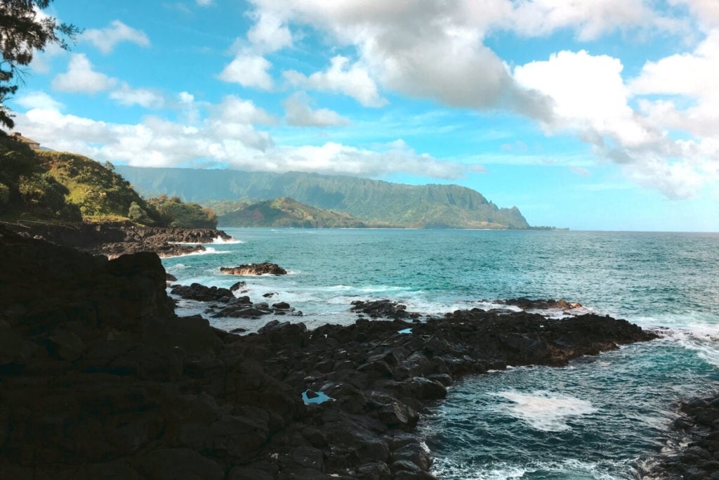 cloudy skies over Queen's Bath Kauai Hawaii with green cliffs in distance