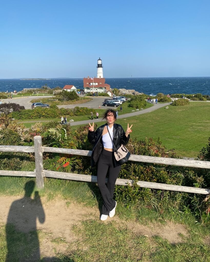 female in a leather jacket standing in front of portland head lighthouse on a windy fall day