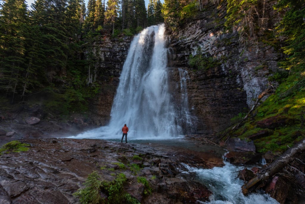 person standing under virginia falls in glacier national park